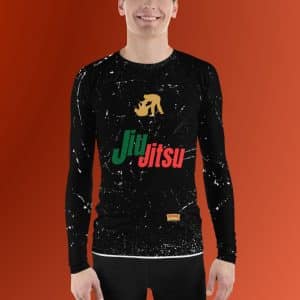 a male model wearing a long-sleeve Jiu Jitsu rash guard with a black base color and white splatter patterns. The center of the rash guard features a gold silhouette of two grappling figures, representing a Jiu-Jitsu move. Below the figures, the text "Jiu Jitsu" is printed in large, bold letters with "Jiu" in green and "Jitsu" in red. At the bottom hem of the rash guard, there is a small, rectangular patch with the "Ringside Report Network" logo. The background of the image is a solid, bright