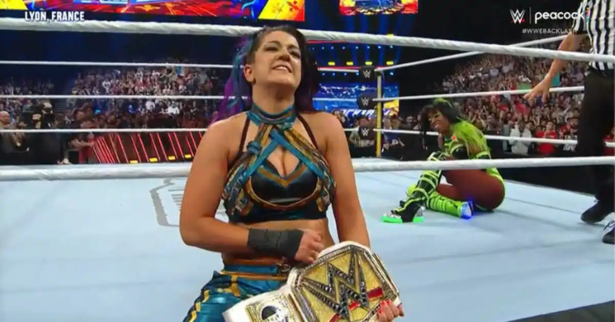 Bayley In The Ring With The Women'S Championship Belt With One Of Her Defeated Opponents In The Background